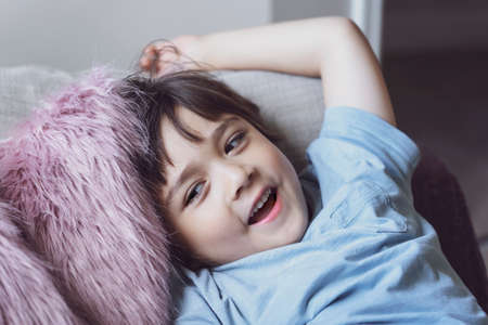 Healhty kid smiling face lying head on fulffy cushion, Happy child boy relaxing at home enjoying time on his own. Positive children conceptの写真素材
