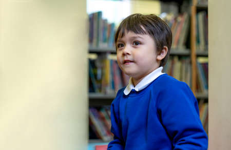 Cropped shot of Preschool kid sittng alone reading a cartoon in the library in the school, child boy...