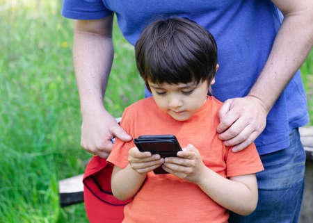 Selective focus father teaching his son using smart phone, Crop shot Dadplaying game with his little boy in the park, Child looking at mobile phone. happy family conceptの写真素材