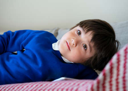 Portrait school kid lying on sofa watching TV after back from school, Adorable Child laying down on couch relaxing in playroom at homeの写真素材