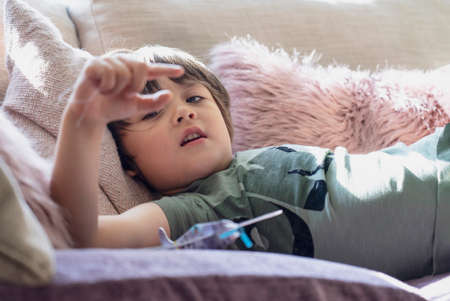 Selective focus happy boy lying on on sofa looking through his finger, High key light child relaxing...