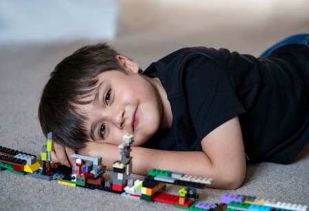 Portrait kid playing plastic blocks, Happy Child boy lying on carpet floor  bluiding his colouful...