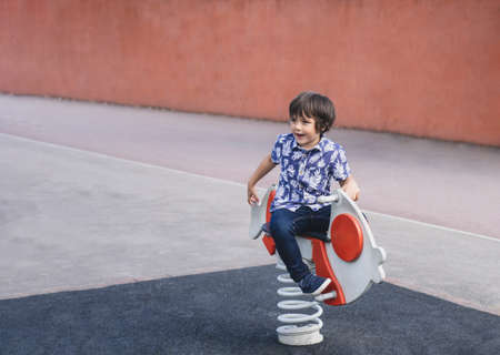 Active kid sitting on rocking chairs in the playground, Happy Child boy having fun playing outdoor...