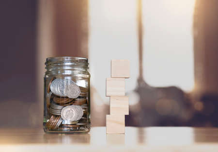 Sterling pound coin and pennies nickels in clear jar with mock up empty stack wooden on table with...