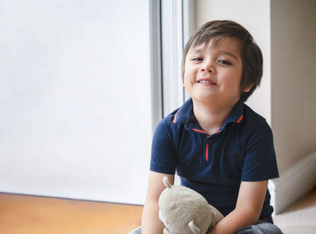 Portrait of happy kid sitting on wooden floor playing with teddy bear, Cute boy play with his soft...