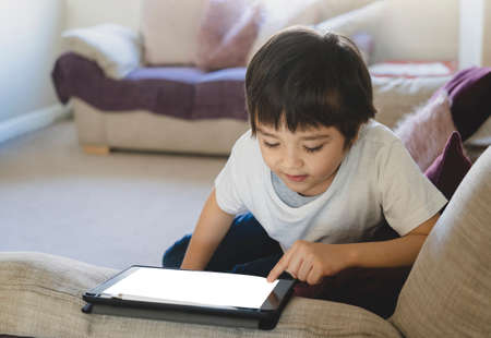 Kid pointing finger on Mock up tablet screen,Child boy lying on sofa relaxing at home watching...