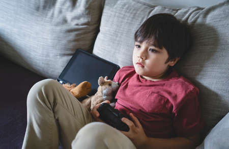 Portrait of kid holding video game or game console. Child playing game online at home, Young boy...