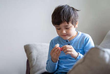Portrait happy kid playing plastick block alone in living room, New normal life style Child boy relaxing at home on weekend. Positive and happiness of children conceptの写真素材