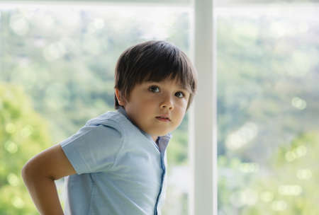 High key light Portrait handsome kid standing next to window looking at camera with smiling face....