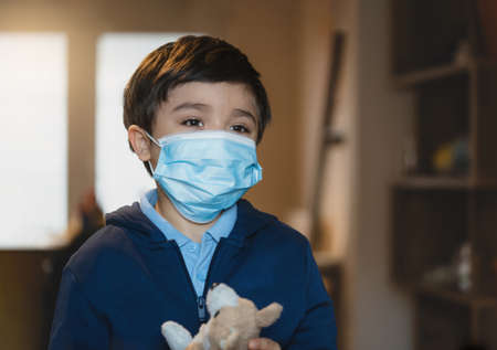 Sick child wearing a protective mask, ill kid in medical face mask standing in living room with sad face,Upset boy standing alone looking deep in thought,Patient isolated in house to prevent infectionの写真素材