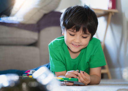 Candid shot Happy kid lying down on floor playing with plastic toy,Positive child playing alone on...