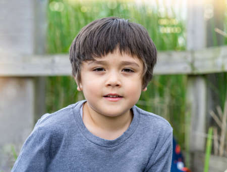 Outdoor portrait cute boy looking at camera with smiling face, Head shot of happy child playing...