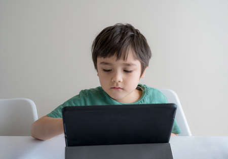 Kid self isolation with bored face using tablet for his homework, Child using digital tablet searching information on internet during covid-19 lock down, Distance, learning online educationの写真素材