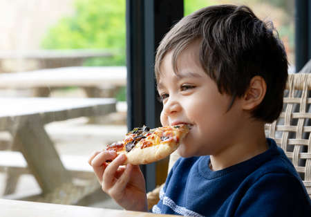 Cropped shot Cute kid boy eating home made pizza in the cafe,  Happy young boy biting off big slice of fresh made pizza in the restaurant, Family happy time conceptの写真素材