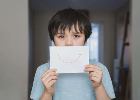 Portrait of bored kid with sad face holding  white paper with smile, Child boy getting bore stay at home during during self-isolation, quarantine. Coronavirus outbreak and flu covid epidemicの写真素材