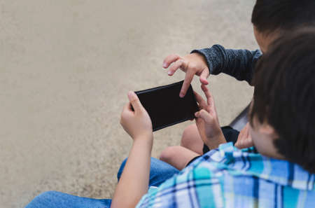 Selective focus two kids playing game on mobile phone, Crop shot top view little boys having fun watching cartoon on cell phone with copy space for text , Friendship conceptの写真素材