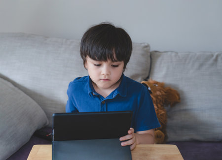 School Kid using tablet for his homework, Child looking at digital tablet with thinking face, Young boy watching cartoon on touch pad, New normal life stye with learning online, Distance educationの写真素材