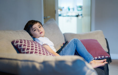 Kid sitting on sofa looking at camera with smiling face.Boy stay at home using tablet learning online lesson from school, Home schooling ,Distance education, E-learning conceptの写真素材