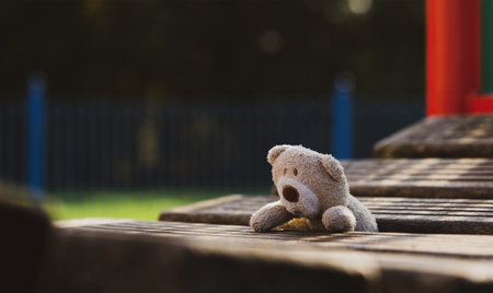 Lost teddy bear lying on wooden bridge at playground in gloomy day, Lonely and sad face brown bear doll lied down alone in the park, lost toy or Loneliness concept, International missing Children dayの写真素材