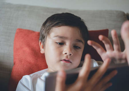 Head shot appy kid watching cartoon on tablet, Candid shot cute boy playing game online with friends on internet, A Child sitting on sofa relaxing at home on weekendの写真素材