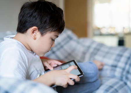 Portrait kid sitting on sofa watching cartoon on tablet,Cute boy playing game online on digital pad,...