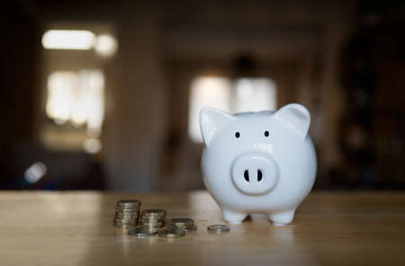 Piggy bank with stack coins on wooden table with blurry background of living roomの写真素材