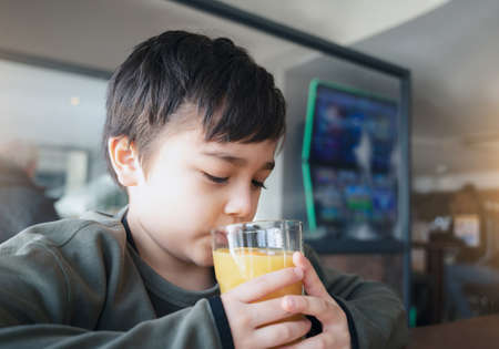 Portrait Young kid drinking fresh orange juice for breakfast in cafe, Happy child boy drinking glass...