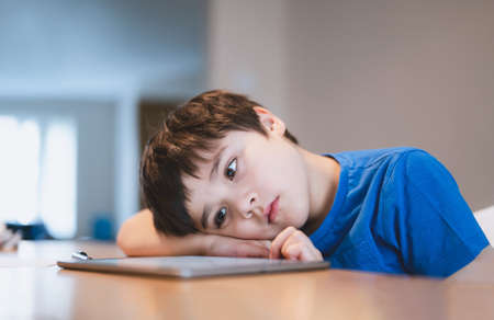 School kid using tablet for homework, Child bored face lying head down looking out deep in thought, Boy learning online class room at home, E-learning or Homeschooling education conceptの写真素材