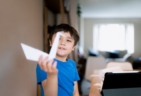 Happy school boy looking at camera with smiling face while showing origami Swan paper. Kid learning paper art origami lesson, Child having fun doing Art and Craft at home, Home schooling conceptの写真素材