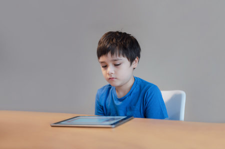 School kid using tablet doing online homework, Child with bored face reading a book on digital reader, Young Boy reading story on e-book, Home schooling , learning online education conceptの写真素材