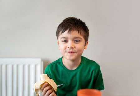 Healhty young boy eating banana, Happy kid having breakfast, Cute Child looking at camera with smiling face.の写真素材