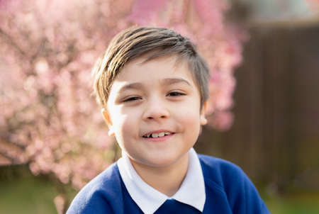 happy young boy looking at camera with smiling face, School kid standing in the front garden