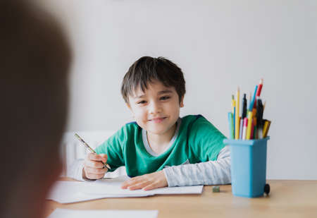 Happy boy using pencil drawing or sketching on paper, Cute kid with smiling face siting on table...