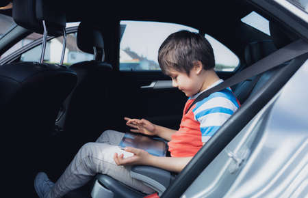 Cinematic portrait Happy young boy using a tablet computer while sitting in the back passenger seat...