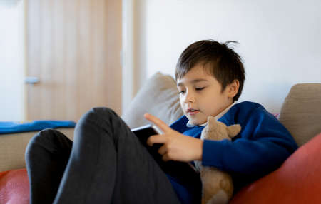 Happy schoolboy playing with dog toy and game online with friend on tablet,Kid using internet...