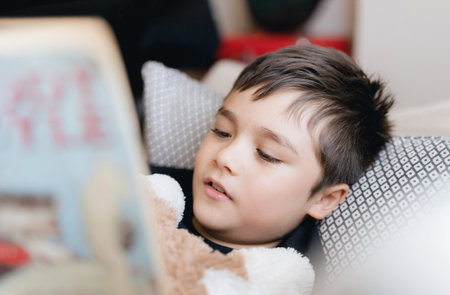 Closeup face School kid reading a book for homework,Head shot Young boy lying on sofa enjoy reading the story in living room,Child relaxing at home on sunny day Spring,Home Schooling,Education conceptの写真素材