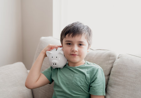 Happy boy holding piggy bank with smiling face. Indoor portrait of a cheerful child showing money saving box.School kid Learning financial responsibility and planning about saving for future conceptの写真素材