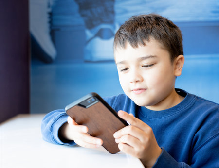 Education concept,School kid using mobile phone readying story from internet,Boy studying online learning at home,Child using cell phone playing game or chatting with friends, Homeschoolingの写真素材