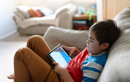 Preteen schoolboy doing homework with digital tablet in living room,Child using gadgets to study. Kid learns online from home,Education learning with new technology for kids.の写真素材