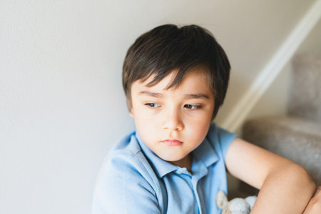 Portrait kid looking out deep in thought, Lonely Child sitting on stairs carpet with thinking face, Childhood and family concept, Selective focus Emotional child portraitの写真素材