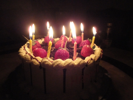 birthday cake with sweet strawberry and light candle in the darkの写真素材