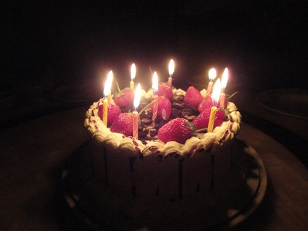 birthday cake with sweet strawberry and light candle in the dark