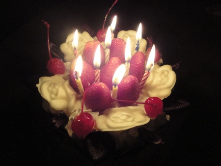 birthday cake with sweet cherry, strawberry,white rose chocolate and light candle in the darkの写真素材