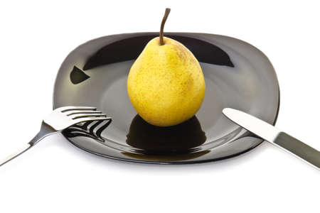 Fresh yellow pear on a black plate with fork and knifeの写真素材