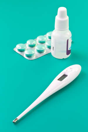 Thermometer, pills and nasal drops closeup on blue background