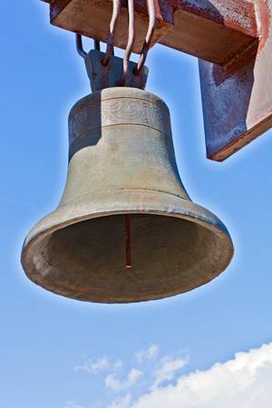 Weathered cast-iron bell against blue sky and cloudの写真素材