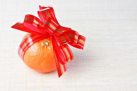 Ripe fresh orange tangerine with red goldish striped bow as a giftの写真素材