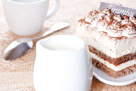 Portion of tiramisu dessert served on a white shaped plate and a cup of coffee with creamの写真素材