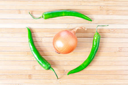 Green chili peppers and onion on a bamboo placematの写真素材