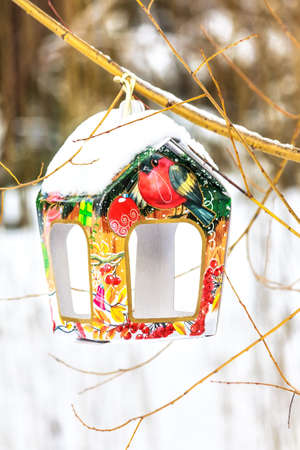 Snow covered colorful birdfeeder on the trunk of tree in a winter parkの写真素材
